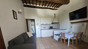 A compact living space with a sofa, a dining table with chairs, a kitchen area with cabinets and a microwave, and a TV mounted on the wall. - FARMHOUSE WITH PANORAMIC POOL IN PERUGIA/ASSISI IDEAL FOR GROUPS FOR 22 PLACES (Perugia)