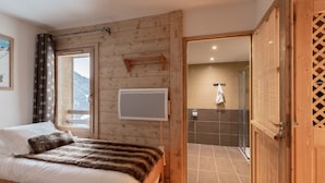 Une chambre à coucher aux murs lambrissés, comprenant un lit, une fenêtre avec des rideaux, un climatiseur fixé au mur et une porte donnant sur une salle de bain.