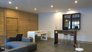 Un salon moderne comprenant une table de baby-foot, un canapé, une table basse et un coin bar avec des tabourets.