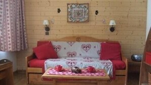 Een knus interieur met een houten wand, een bank met rode kussens, een tafel met een geruit tafelkleed en twee wandlampen.