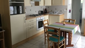 A compact kitchen with a gas stove, oven, sink, and a dining area with a table and chairs. - Maisonette 2 persons   (Biscarrosse)