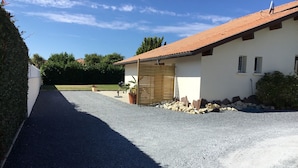 A gravel driveway leading to a building with a tiled roof, a wooden gate, and a small garden area with plants and rocks. - Maisonette 2 persons   (Biscarrosse)