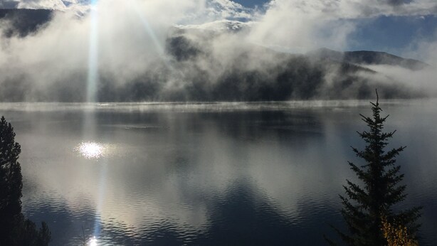 Un lago tranquilo con montañas al fondo y un cielo despejado.