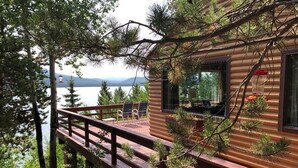 Una cabaña con terraza de madera que da a un lago, rodeada de árboles.
