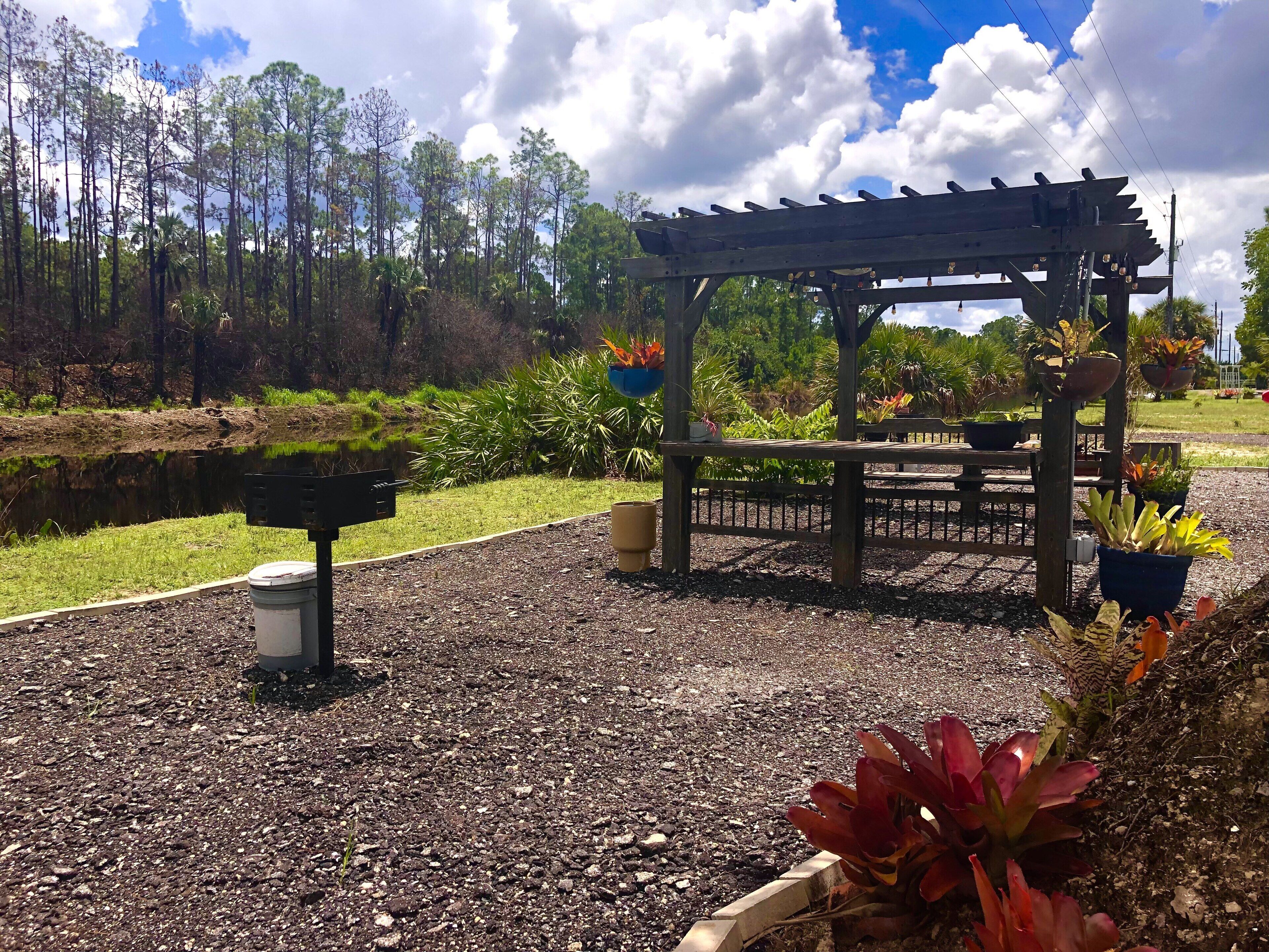 A garden with a wooden pergola, a pond, and various potted plants.