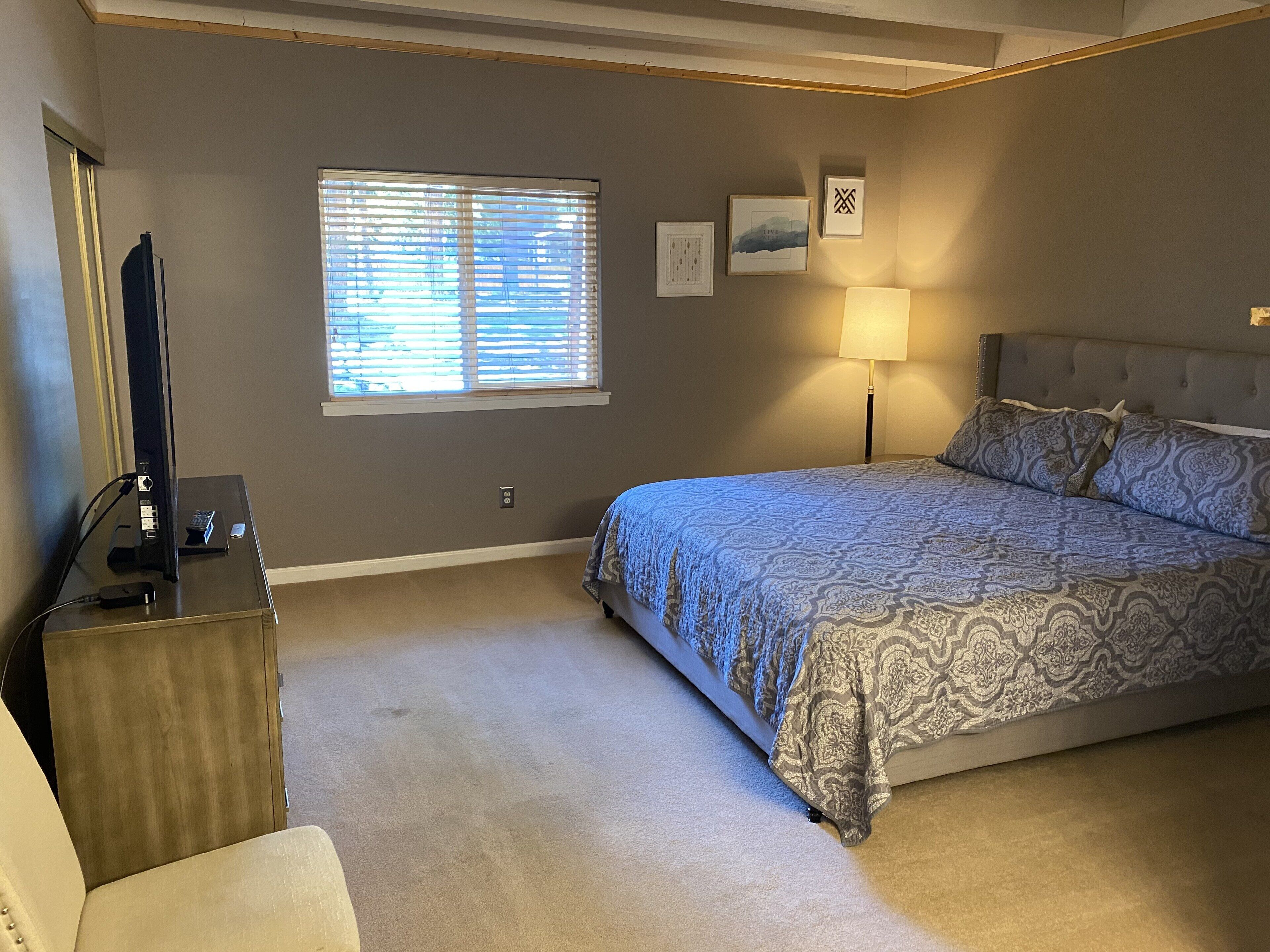 A bedroom with a bed, a desk with a computer, a lamp, and a window with blinds.