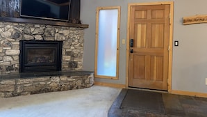 A stone fireplace with a TV above it, a wooden door, and a stone wall. - 3 Bedroom Incline Village Retreat Next to Championship Golf Course (IVGID)