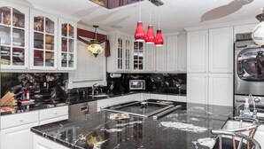 Una cocina moderna con armarios blancos, encimera de mármol negro, horno integrado y una lámpara colgante roja.