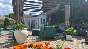 Un patio al aire libre con una pérgola, plantas en macetas y una mesa cubierta con mantel verde.