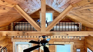 Interior de madera con techo inclinado, ventilador de techo y ventana con cortinas.