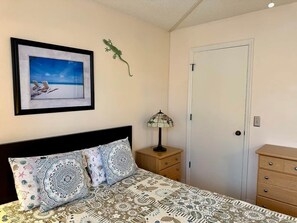 Une chambre à coucher comprenant un lit, une table de chevet, une lampe, une commode, une porte et un tableau encadré accroché au mur.