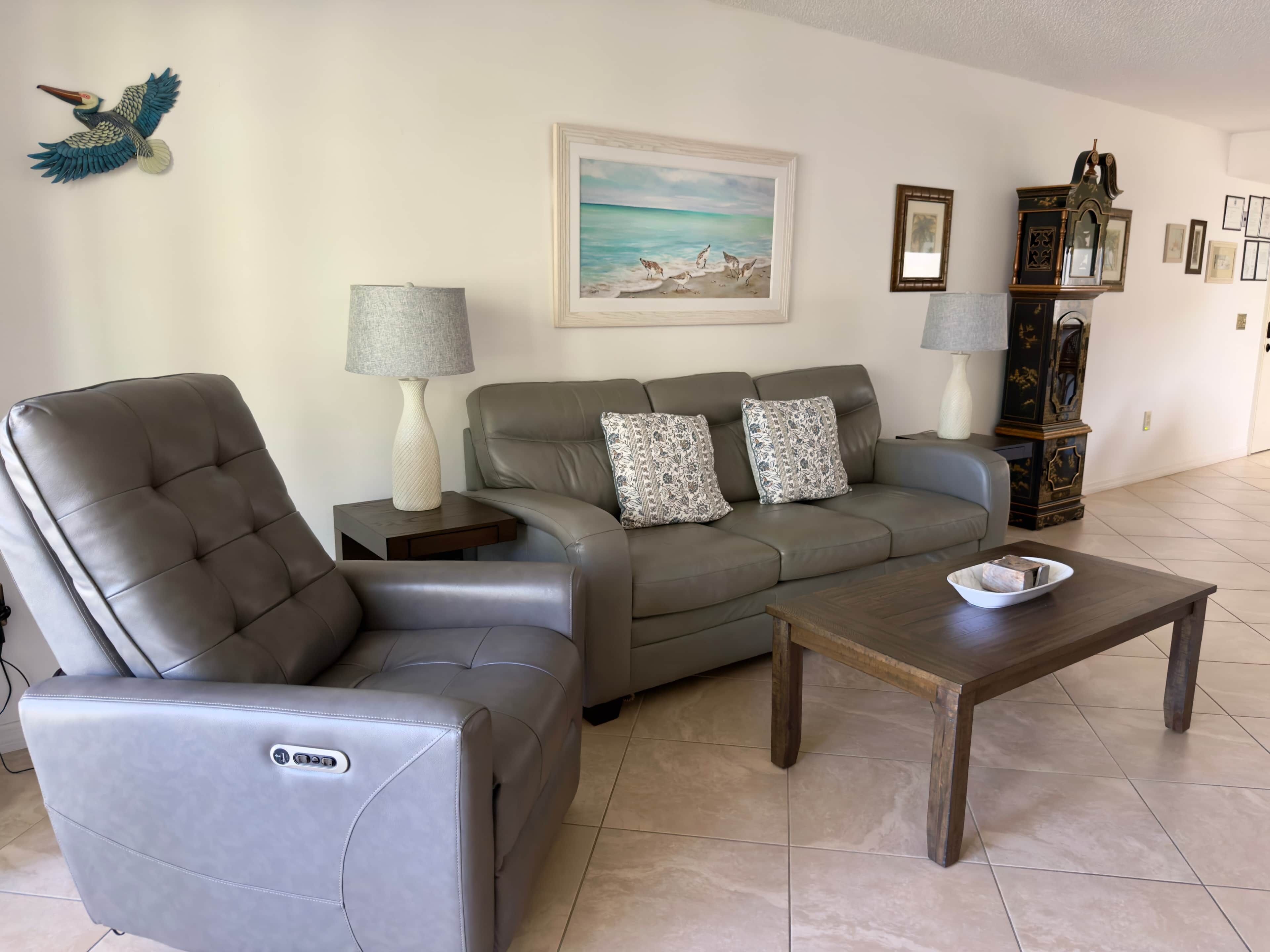 Una sala de estar con un sofá de cuero, un sillón reclinable, una mesa de centro y una lámpara.