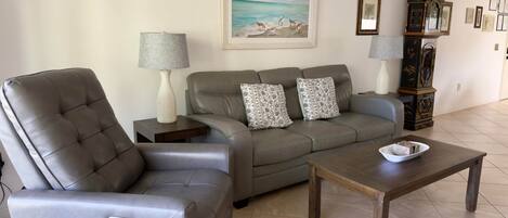 Una sala de estar con un sofá de cuero, un sillón reclinable, una mesa de centro y una lámpara.