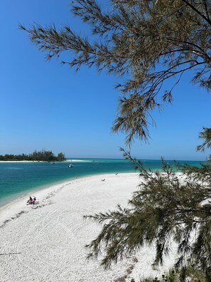 Una playa de arena blanca, agua turquesa cristalina y cielo azul despejado.