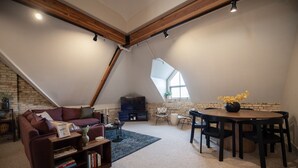 Un soggiorno in stile loft con soffitto spiovente, un divano, un tavolino, una TV e un tavolo da pranzo con sedie.