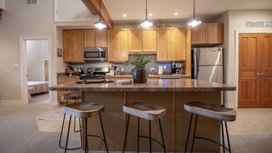 Una cucina moderna con mobili in legno, una grande isola con sgabelli da bar, elettrodomestici in acciaio inossidabile e luci a sospensione.