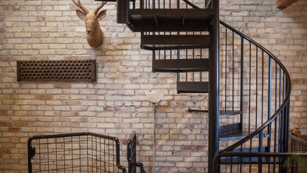 Una scala a chiocciola con ringhiere in metallo, un muro in mattoni e una testa di animale decorativa montata sulla parete.