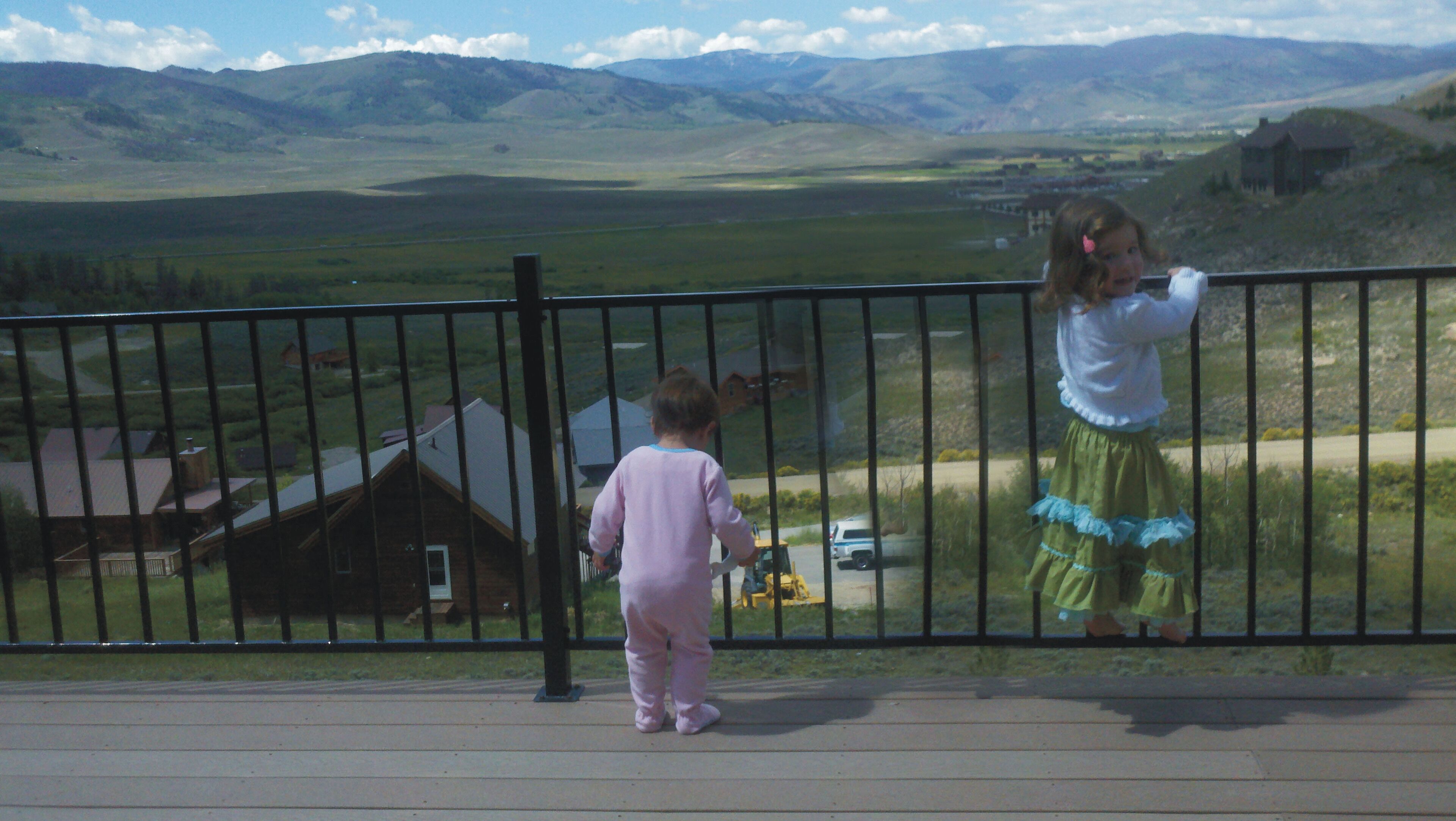 Un niño y un adulto de pie en un balcón con vistas a un paisaje rural, incluyendo casas y montañas.