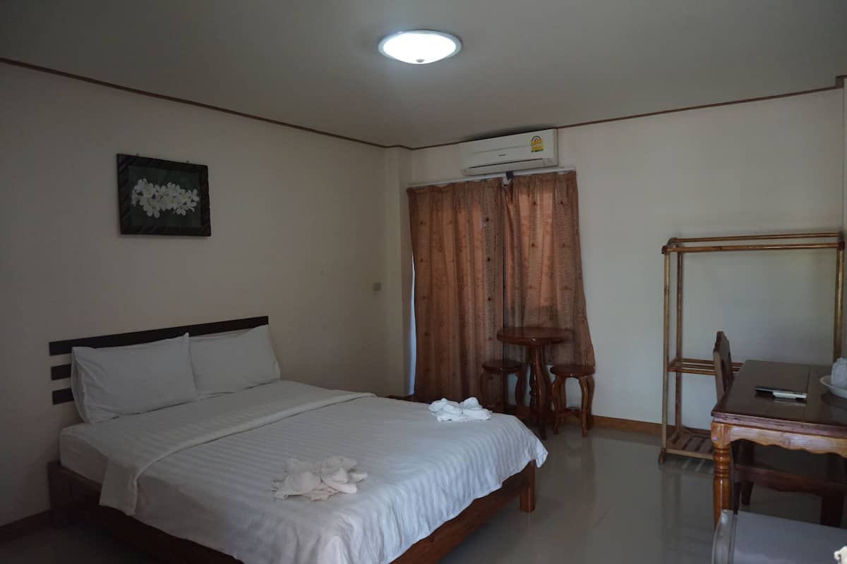 A hotel room with a bed, a small table with chairs, a mirror, an air conditioning unit, and a framed picture on the wall.
