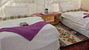 Une pièce aménagée comme une tente, avec deux lits, chacun recouvert d’une couverture violette. On y trouve deux tables de chevet avec des lampes et une bouilloire.