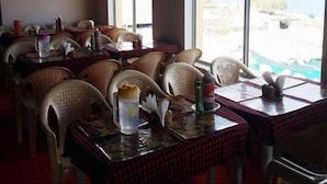 Un restaurant avec des chaises et des tables en osier, de grandes fenêtres offrant une vue sur la mer.