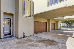 A building with a covered parking area, a garage door, and a door with a number plate. - The Jamerican (Houston)