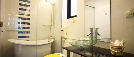 A modern bathroom with a glass sink, a white toilet with a yellow seat, and a glass shower enclosure.