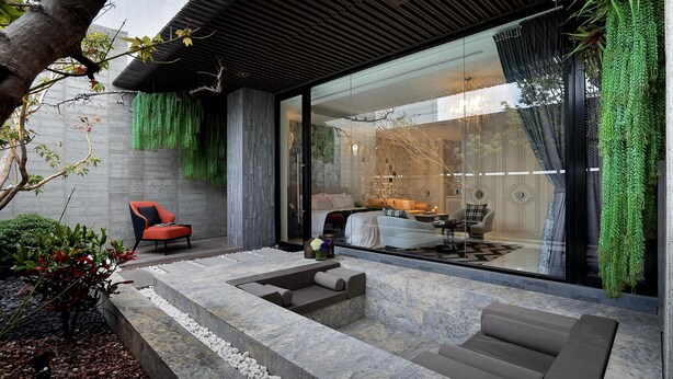 A modern outdoor seating area with a stone bench, a red chair, and a glass wall leading to a room with a bed and a desk. - Ease Motel Taichung (Taichung)
