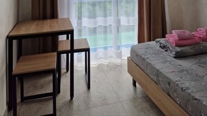 A room with a bed, a table, a chair, a TV mounted on the wall, and a window with curtains.