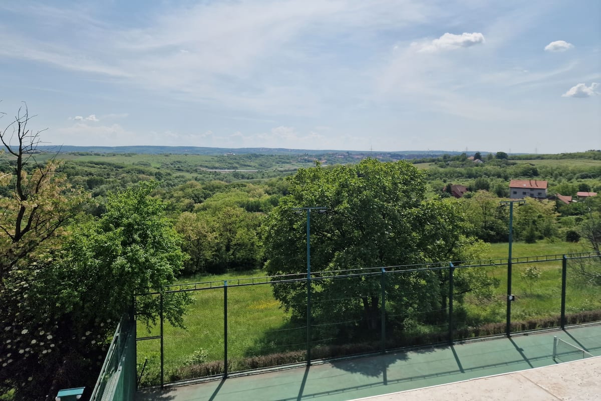 A tennis court with a view of a green landscape and distant buildings.