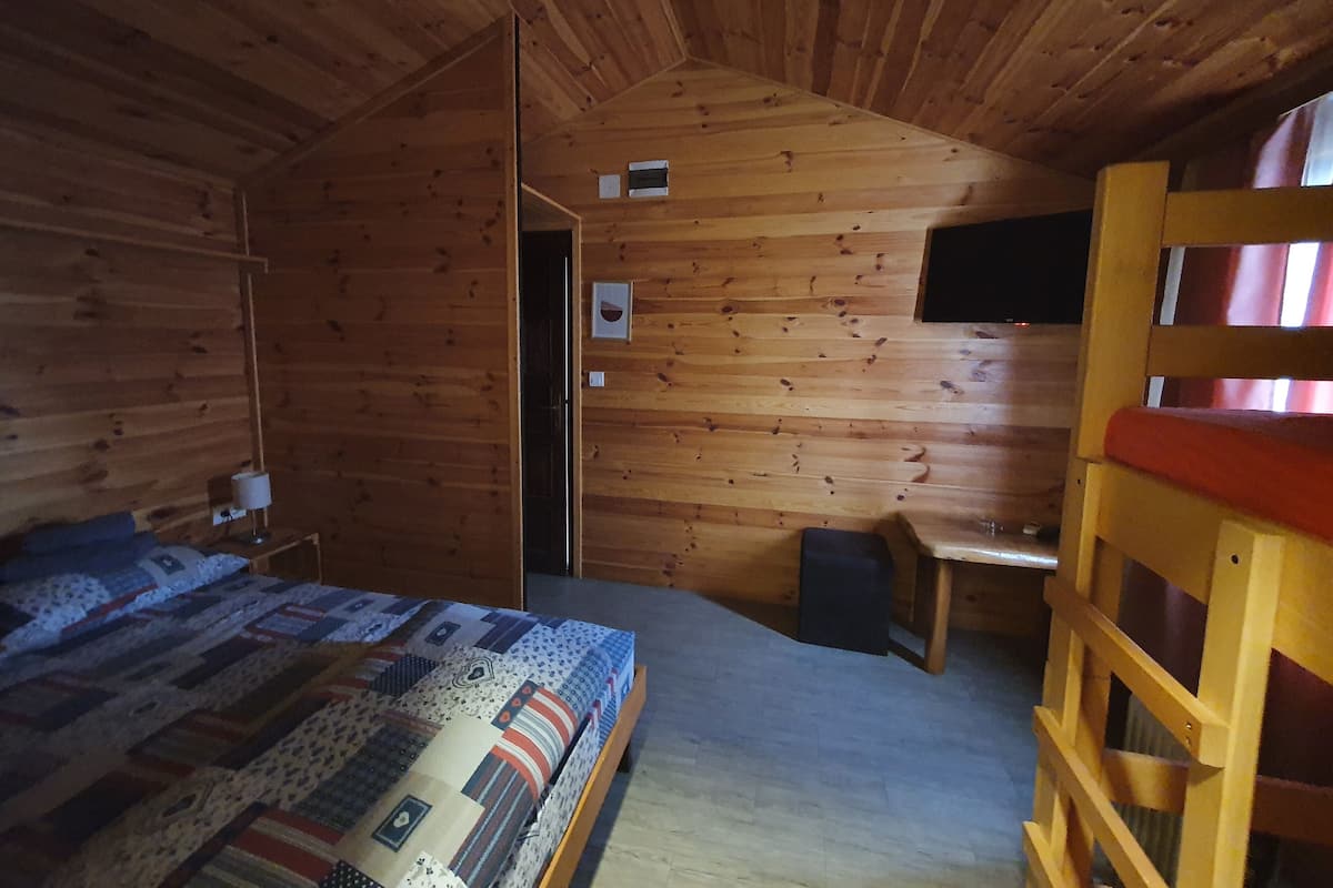 A wooden cabin room with a bed, a desk, and a bunk bed.