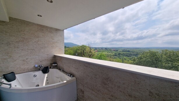 A modern bathroom with a freestanding bathtub, a shower, and a large window offering a scenic view of a green landscape. - Green Set (Belgrade)