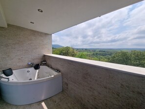 A modern bathroom with a freestanding bathtub, a shower, and a large window offering a scenic view of a green landscape.