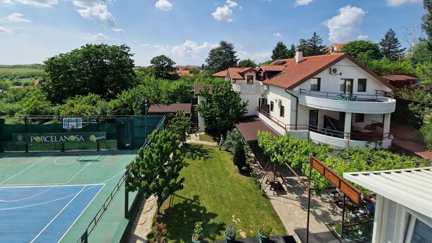 A residential area with a tennis court, a house with a balcony, and surrounding greenery.