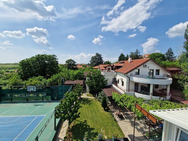 A residential area with a tennis court, a house with a balcony, and surrounding greenery.
