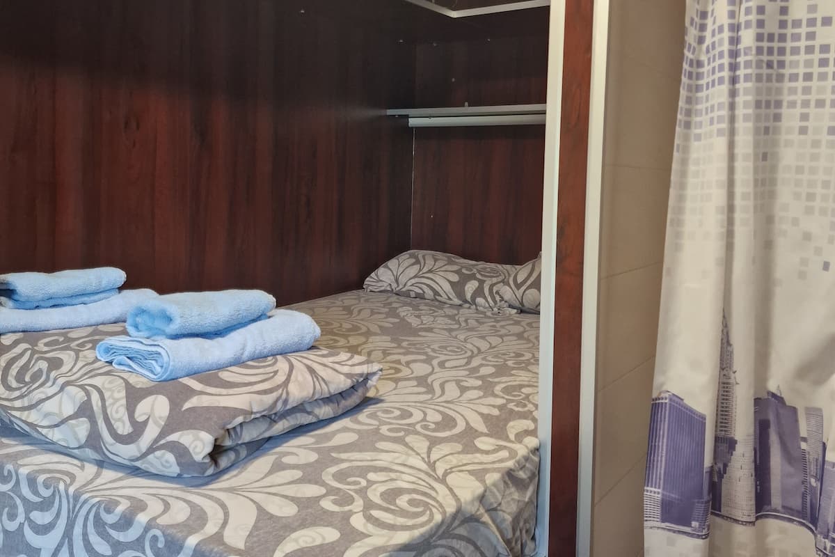 A bedroom with a bed, a wooden wardrobe, and a bathroom with a curtain.