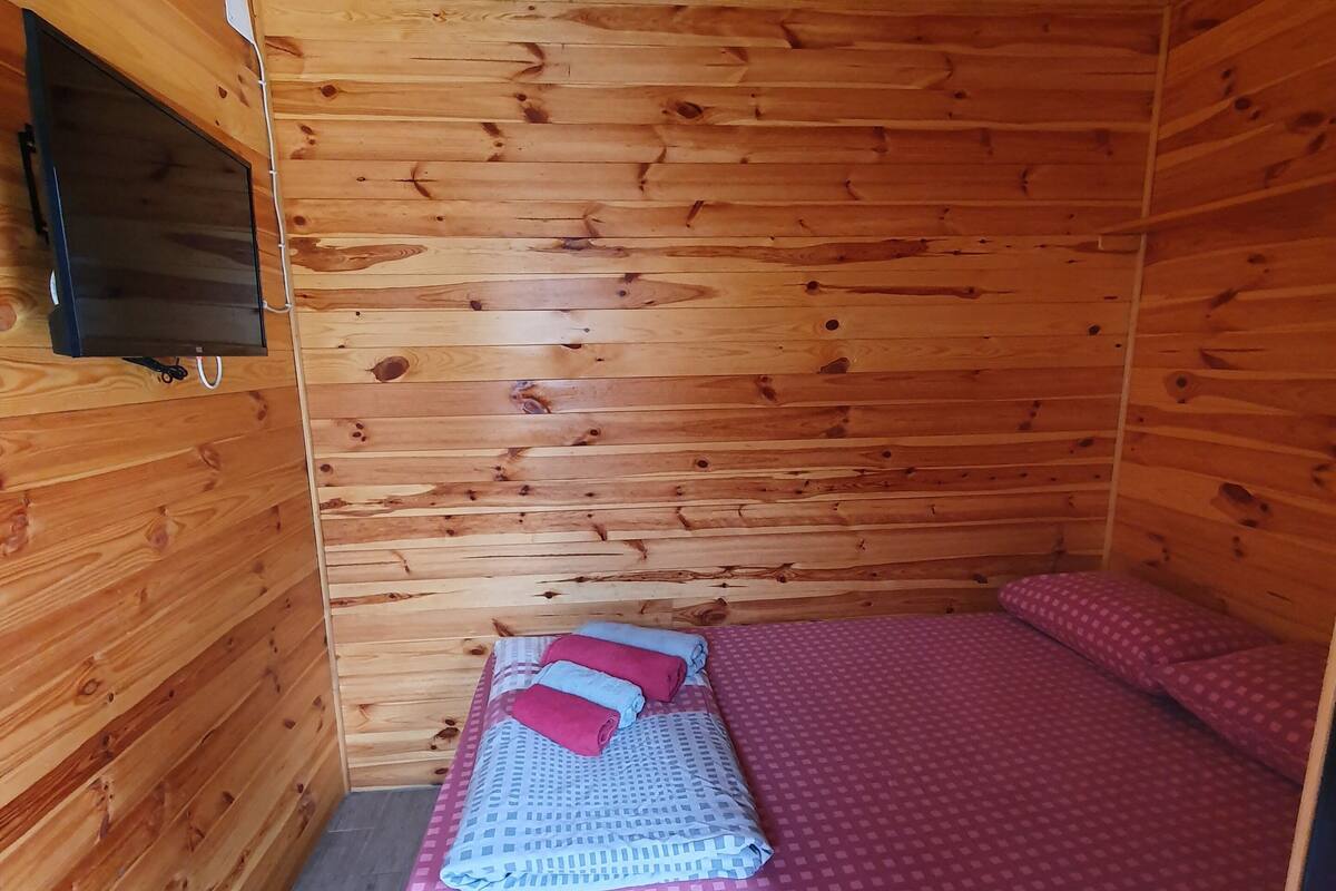 A wooden cabin room with a bed, pillows, and a mounted television.