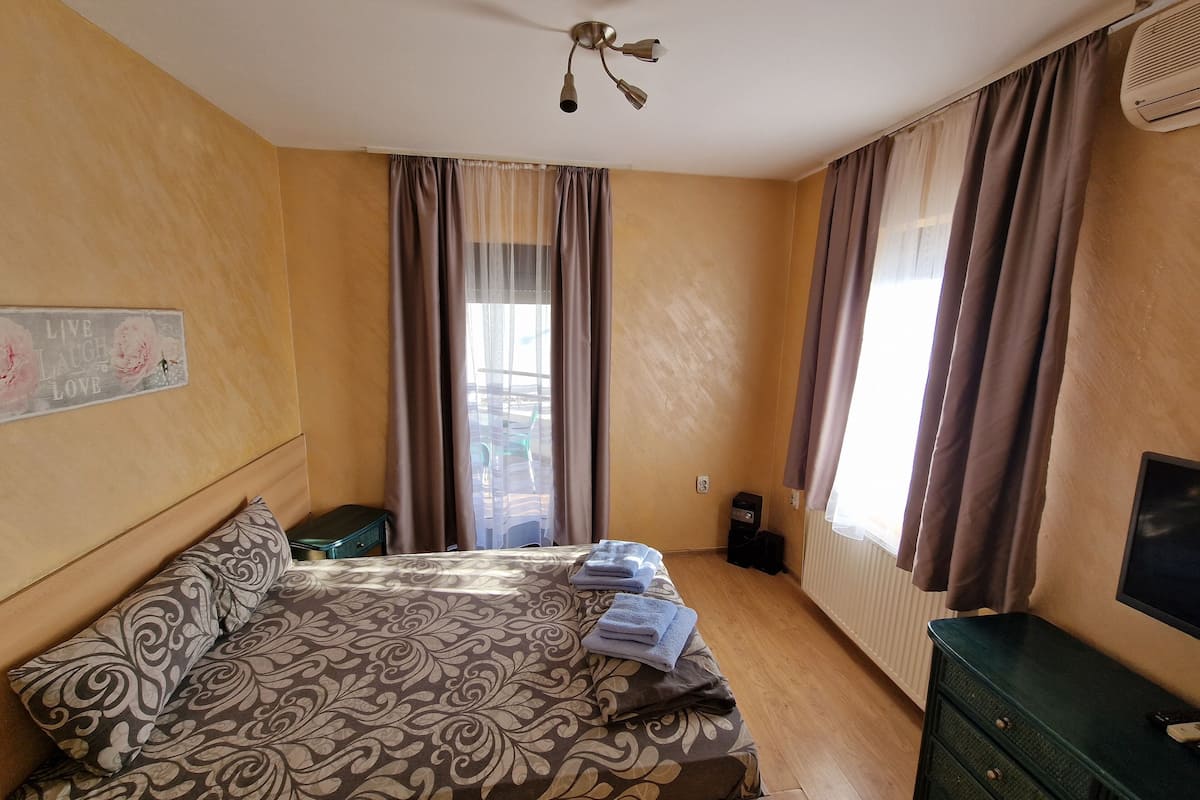 A bedroom with a bed, a dresser, a ceiling fan, a radiator, and a window with curtains.