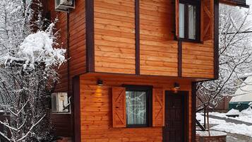 Una casa de madera de dos pisos con cimientos de ladrillo, fachada de madera y techo cubierto de nieve.