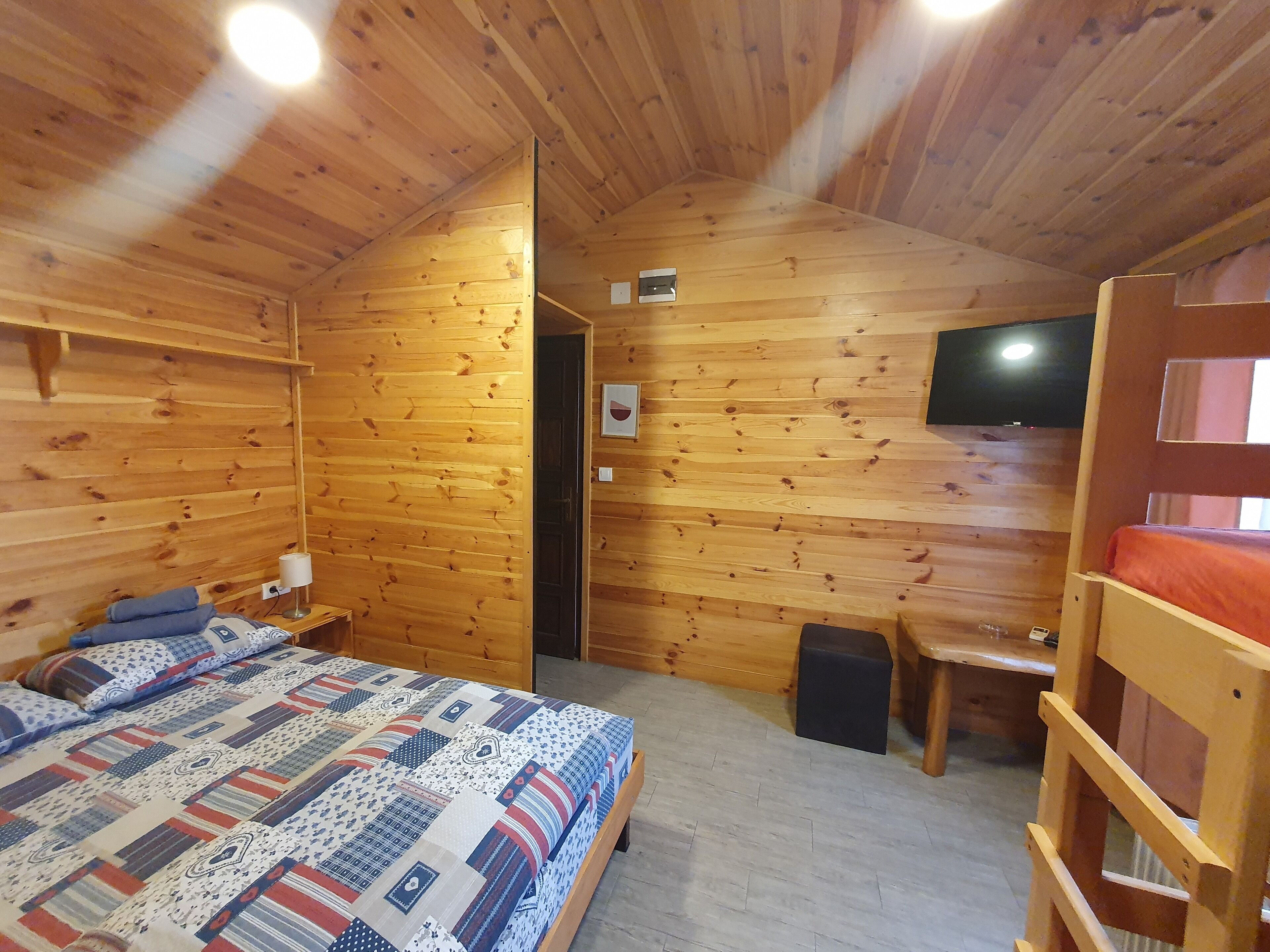 Une pièce chaleureuse, aménagée dans une cabane en bois, avec un lit, un bureau et un téléviseur fixé au mur.