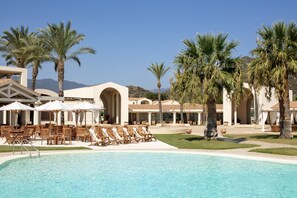 Ein Poolbereich eines Resorts mit Liegestühlen und Sonnenschirmen, Palmen und einem Gebäude mit Bogenportal.