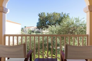 Ein Balkon mit zwei Stühlen und einem Tisch, mit Blick auf einen Garten mit Bäumen und einem Gebäude im Hintergrund.