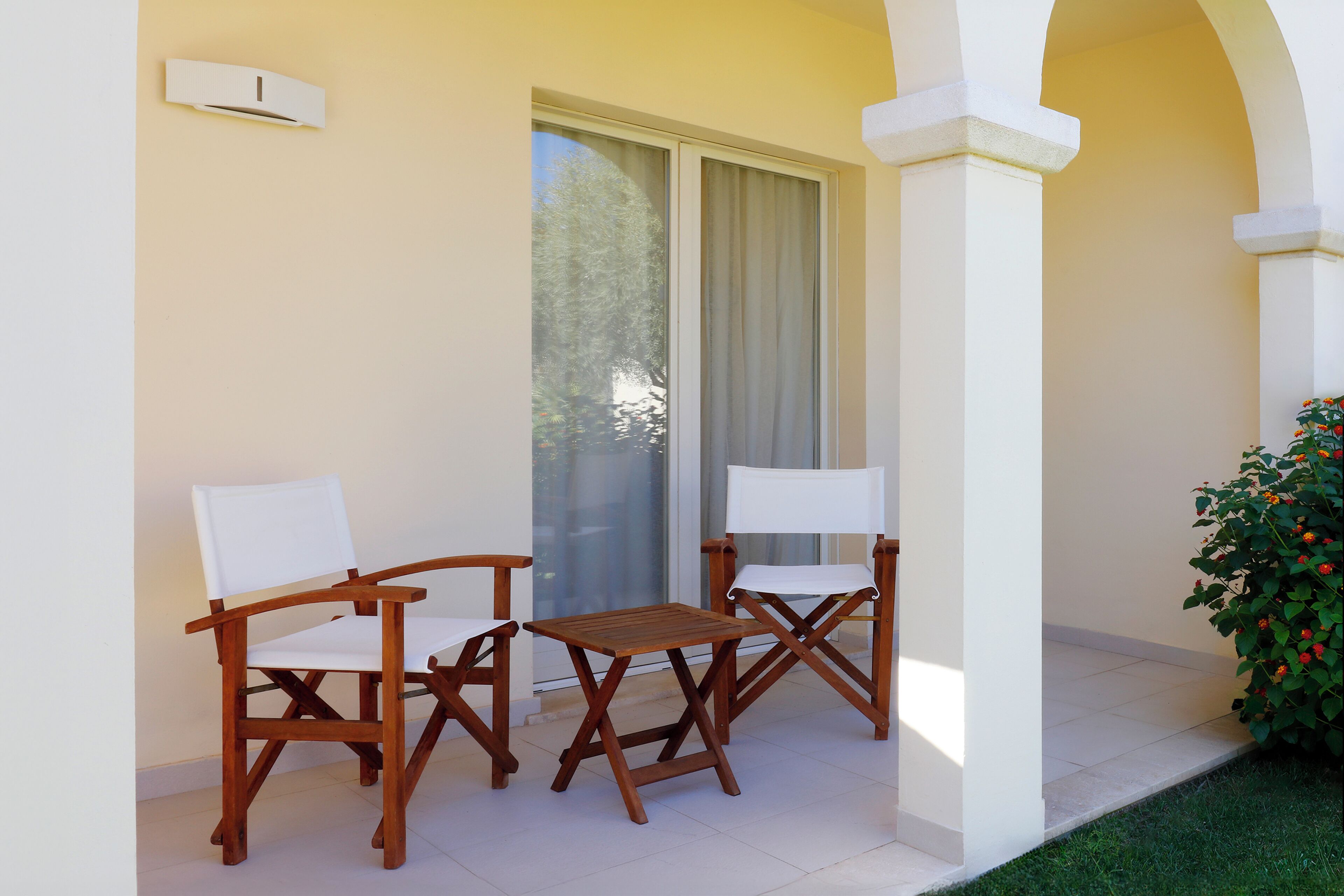 A patio with two wooden chairs and a small table, a sliding glass door, and a potted plant.