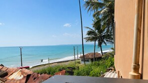 A balcony with a view of the beach, palm trees, and a small building. - Villa Yuvin (Dondra)
