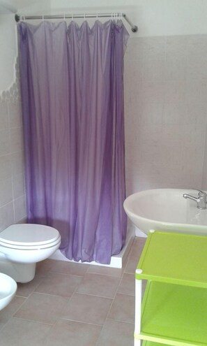 A bathroom with a white toilet, a purple shower curtain, a white bathtub, and a green shelf. - Alma bed & breakfast (Sennariolo)