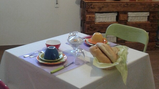 A dining table set with plates, cutlery, and a sandwich, with a rustic wooden shelf and a window in the background. - Alma bed & breakfast (Sennariolo)