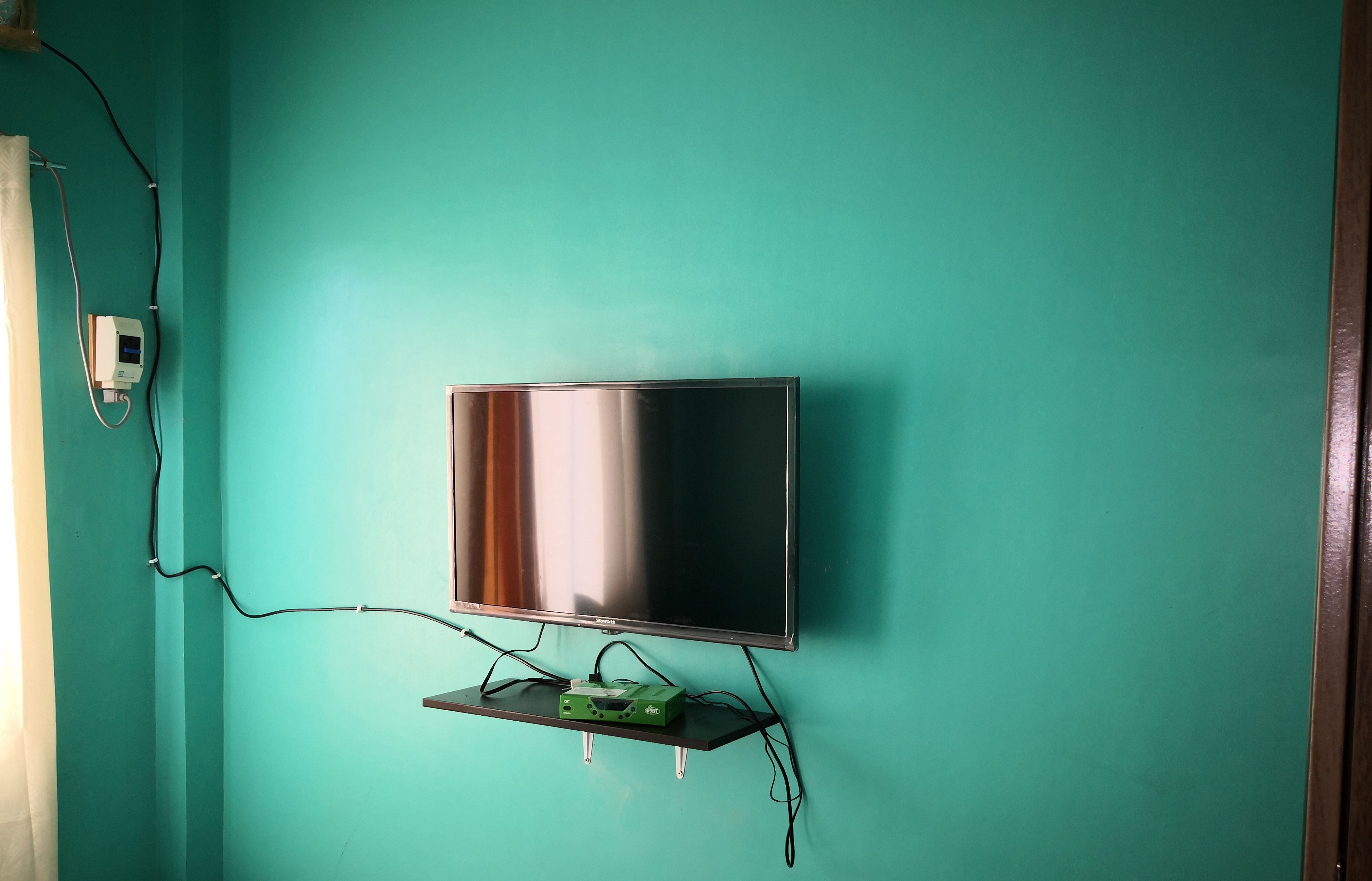 A television mounted on a teal wall with a cable box below it.