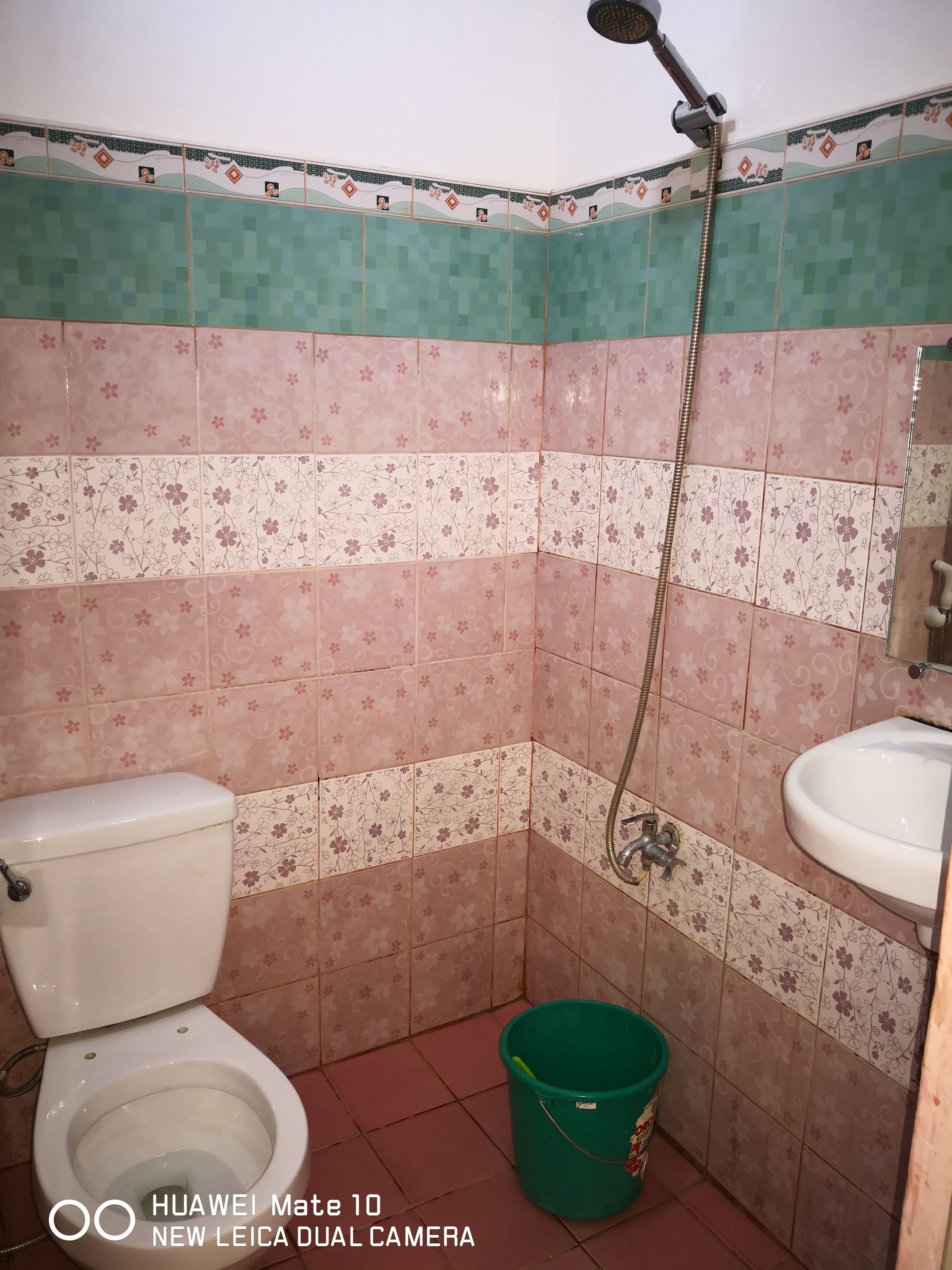 A bathroom with a toilet, sink, shower, and a green bucket.