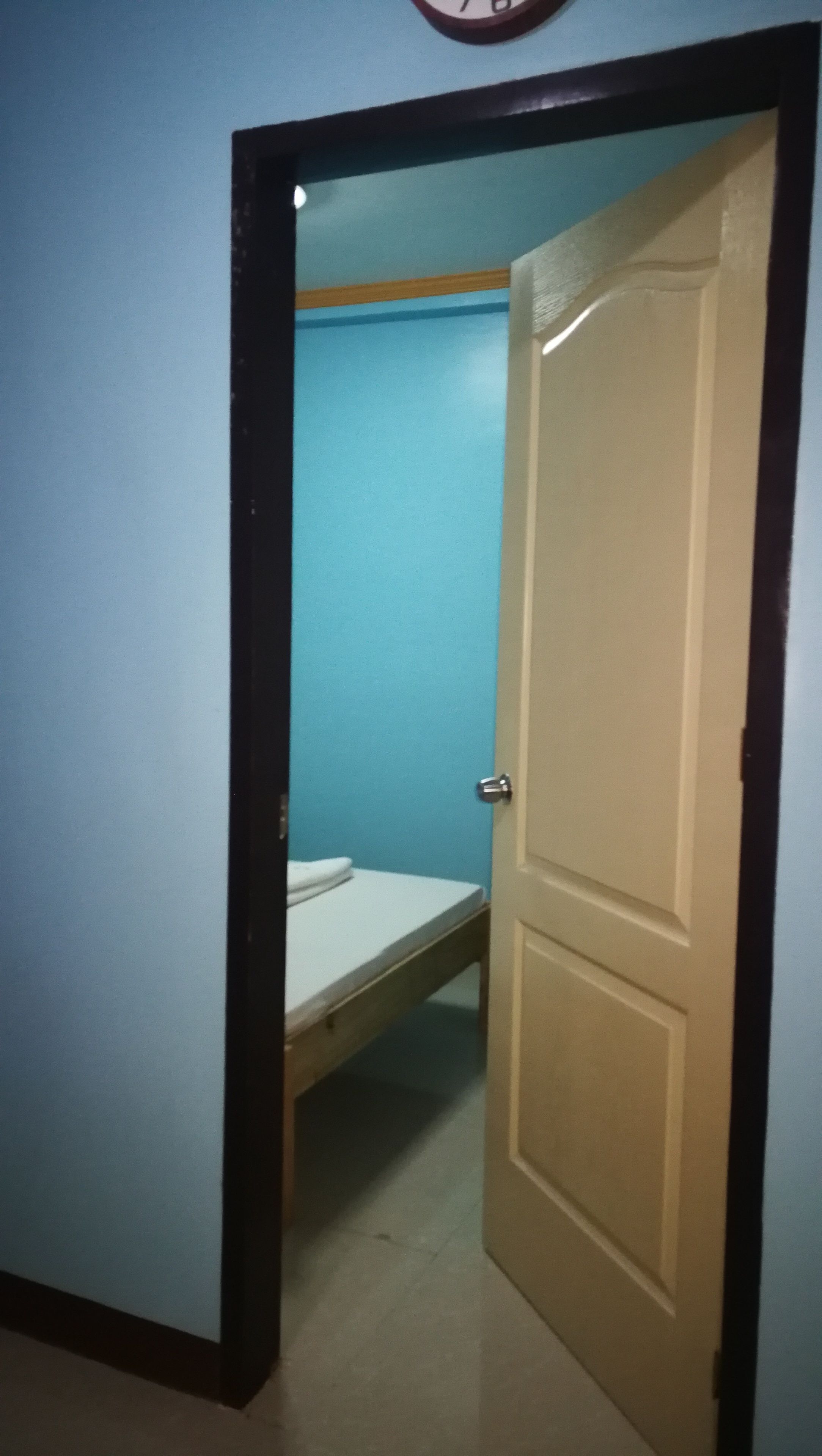 Een kamer met een bed, een deur en een wandklok.