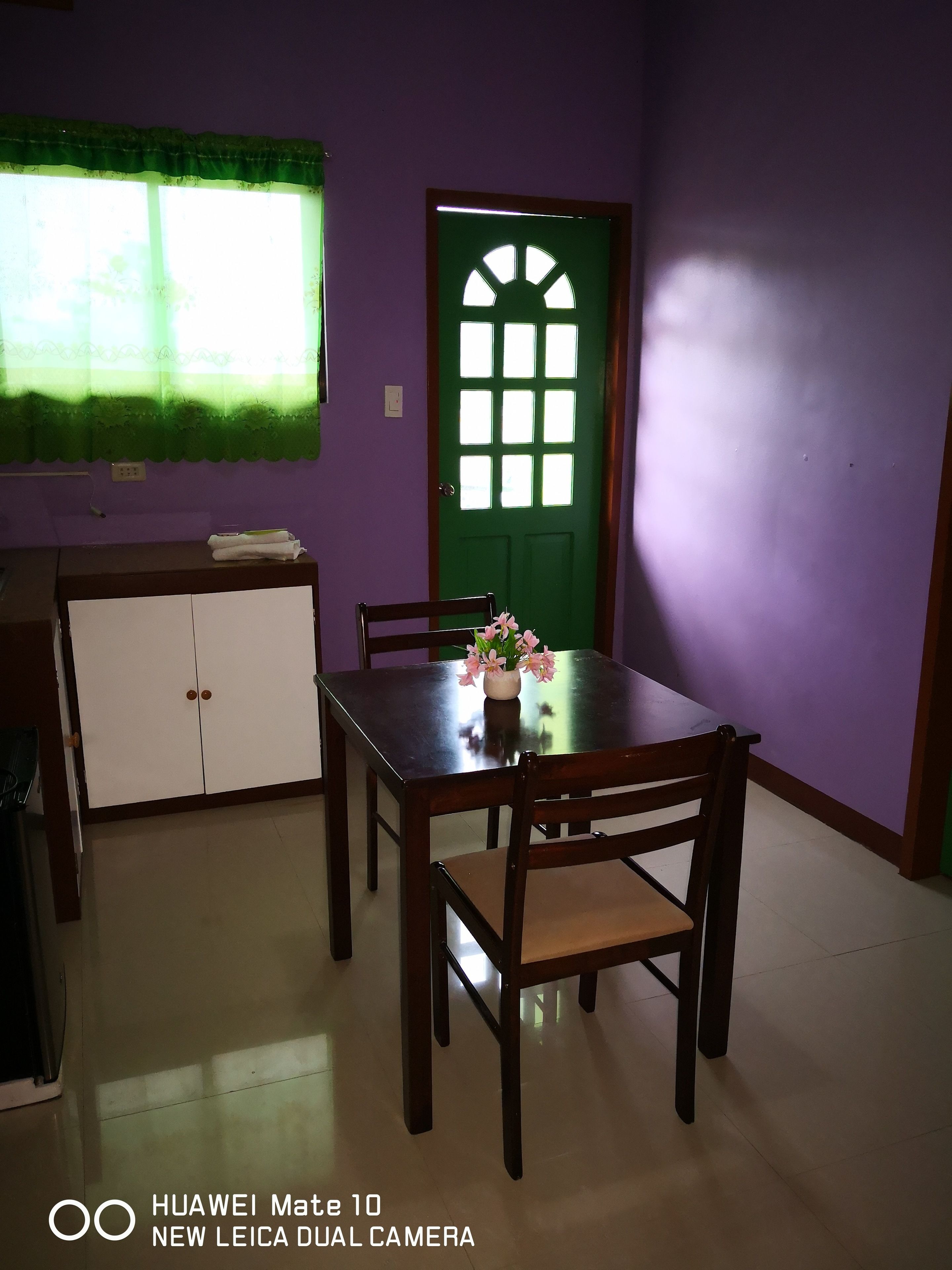 Een eetruimte met een groene deur, een wit kastje en een tafel met stoelen.